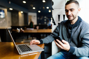 Smiling businessman sending a text message with laptop beside at the cafe. Man send or read message looking at phone