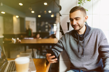 Fototapeta na wymiar Young man drinking coffee in cafe and using phone with smile