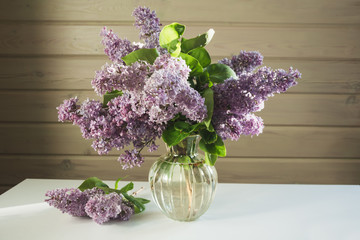 A bouquet of fresh lilacs in a beautiful glass vase on a white table in a farmhouse.