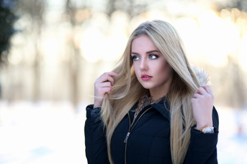 Portrait of a young blond woman with long healthy hair in winter park.