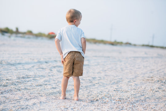 back view of little boy walking at the beautiful beach at sunset
