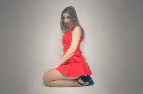 Sexy girl in short red dress and high heels shoes is sitting on the floor and looking ahead isolated.