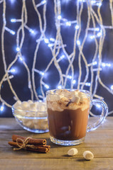 Hot chocolate, cinnamon sticks and marshmallow on the background of burning garlands, Christmas decorations, close up