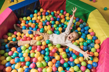Fototapeta na wymiar high angle view of happy little boy lying in pool with colorful balls