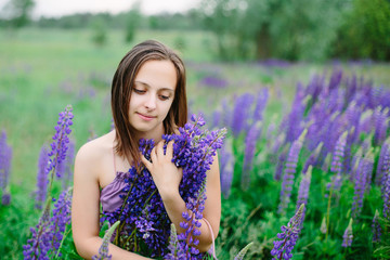 Beautiful young girl in ultra violet dress holding a bouquet of lupine at sunset on the field. The concept of nature and romance.