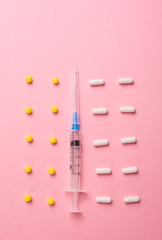 Creative concept Illness: syringe, vitamins and tablets on pink background