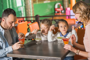 family with two children eating tasty desserts in cafe at entertainment center