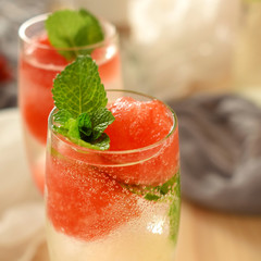 Sparkling cocktail with watermelon and melon ball-shaped pieces and ice and decorated with mint