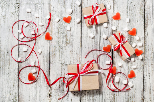 Valentines Day candy hearts marshmallows and box of gifts in craft paper over white wooden background