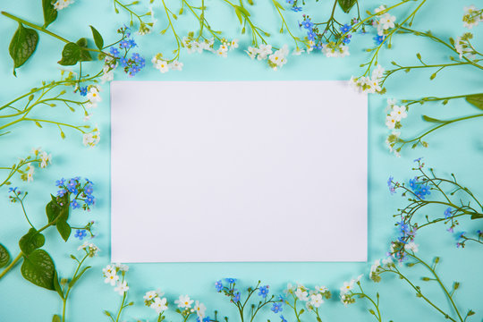 Clear sheet of white paper surrounded with blue and white little flowers on light mint background.