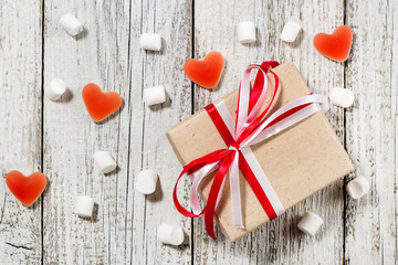 Valentines Day candy hearts marshmallows and box of gifts in craft paper over white wooden background