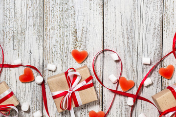 Valentines Day candy hearts marshmallows and box of gifts in craft paper over white wooden background