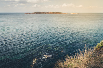 View from the cliff with dry grass at the sea and the island. Toned.