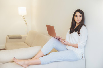 Thoughtful beautiful woman plans projects while sits at comfotable sofa with laptop computer, thinks about learning or preparing course wok. Restful female enjoys online communication at home