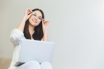 Positve female being glad to finish her course paper, works on laptop computer. Creative female web designer watches video with new graphic ideas, sits against white background. Technology concept