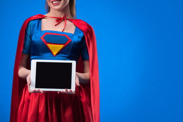 partial view of woman in superhero costume showing tablet with blank screen isolated on blue