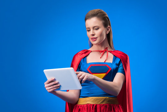 portrait of caucasian woman in superhero costume using tablet isolated on blue