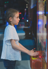 Little girl playing claw crane in theme park.