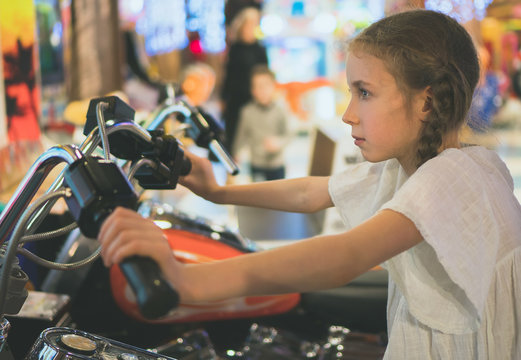 Little girl playing motorbike simulator game in theme park.