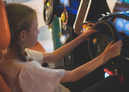 Little girl playing racing simulator game in theme park.