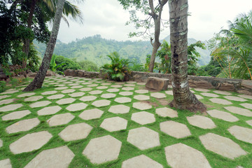 Beautiful tropical landscape with courtyard decorated with stone slabs and green lawn. Landscaping in Asia with bush, coconut trees and lush on green hills