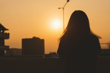 A girl's back with the background of amazing scene of sunset between sky with city view from top of the floor.