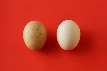 An egg with a yellow brown spot and a clean white egg on the red background - 189612190