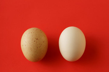 An egg with a yellow brown spot and a clean white egg on the red background