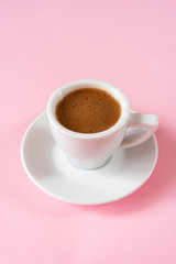  A cup of espresso with foam in a white cup on a white saucer on a vivid pink background. Place for text. Close up.  