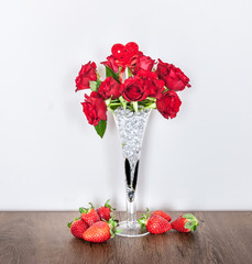 Centerpiece with red roses and strawberries on Valentine's Day on a wooden table