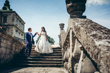 Full-length wedding portrait of the adorable newlywed couple going down the old castle strais. The...
