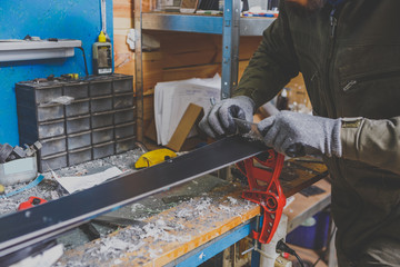 A male worker in a ski service workshop repairs the sliding surface of the skis. Close-up of a hand...