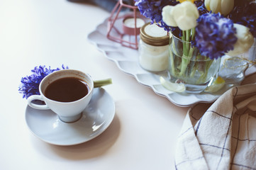 spring morning at home with cup of coffee, candles and flowers on white table. Seasonal decoration, cozy living, hygge concept