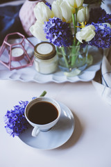 spring morning at home with cup of coffee, candles and flowers on white table. Seasonal decoration, cozy living, hygge concept