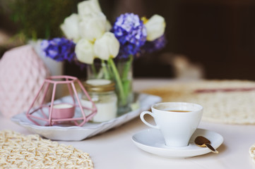 Morning coffee, spring decorations at home on the table in modern scandinavian style with flowers and aromatic candles. Slow living and hygge concept