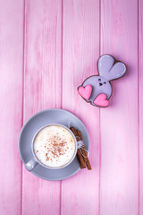 Coffee cappuccino with cinnamon and gingerbread rabbit with heart on a pink wooden background. Happy Valentine's Day!