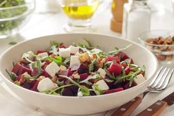 Healthy organic salad with beet, arugula, feta, walnut and olive oil mustard dressing in ceramic bowl.