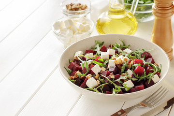 Beetroot salad with arugula, feta and walnuts in the bowl on white wooden table.