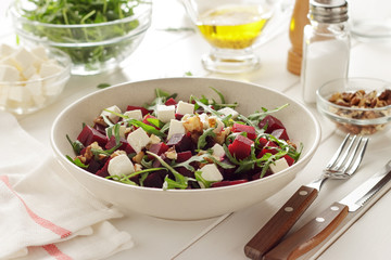 Vegetarian salad with beetroot, arugula, walnuts and cheese in ceramic plate on white kitchen table.