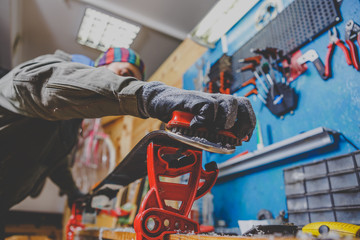 A man in work clothes, repairman in workshop ski service repairing the sliding surface of skis,...