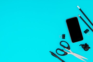 Modern concept background. Business workspace with black accessories: mobile phone, pencil, pen, scissors on blue background. Flat lay. Top view.