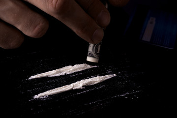 Drug addiction. Junkie man sniffs a line of cocaine through a dollar. Black background. Narcotics concept. - obrazy, fototapety, plakaty