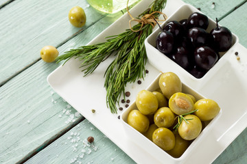 Wooden background with  black olives, green olives, olive oil, fresh rosemary and spices.