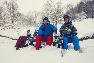 Fototapeta na wymiar Smiling snowboarders are drinking coffee from thermos in the forest