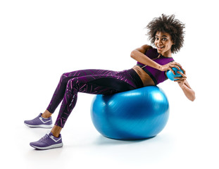 Smiling sporty girl doing fitness exerrcise on gymnastic ball. Photo of young african girl in sportswear on white background. Sports