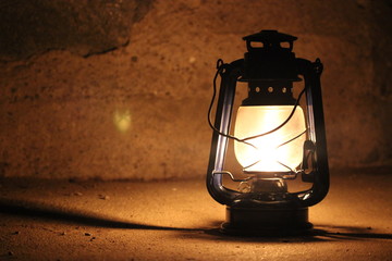 Kerosene lamp lights in a dark near a stone wall.