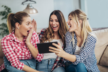 Three best friends using digital tablet together. Women sitting on sofa having fun surfing on the internet using smart digital pc tablet modern device
