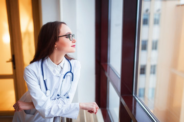 medical student beautiful young girl with glasses, in the university near the window. The doctor smiles after the end of the working day