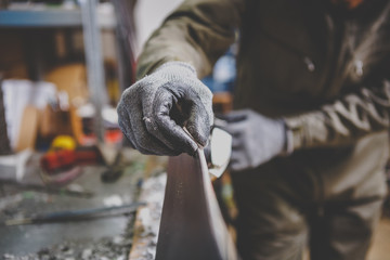 A man repairman in workshop ski service repairing the sliding surface of the ski at Ski vise. In hands of instrument Final edge sharping by gummy stone. Theme ski repair and maintenance of equipment