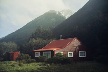 Fototapeta na wymiar Imagen de casa roja en medio de la montaña con cielo nuboso. Paisaje de montaña.
